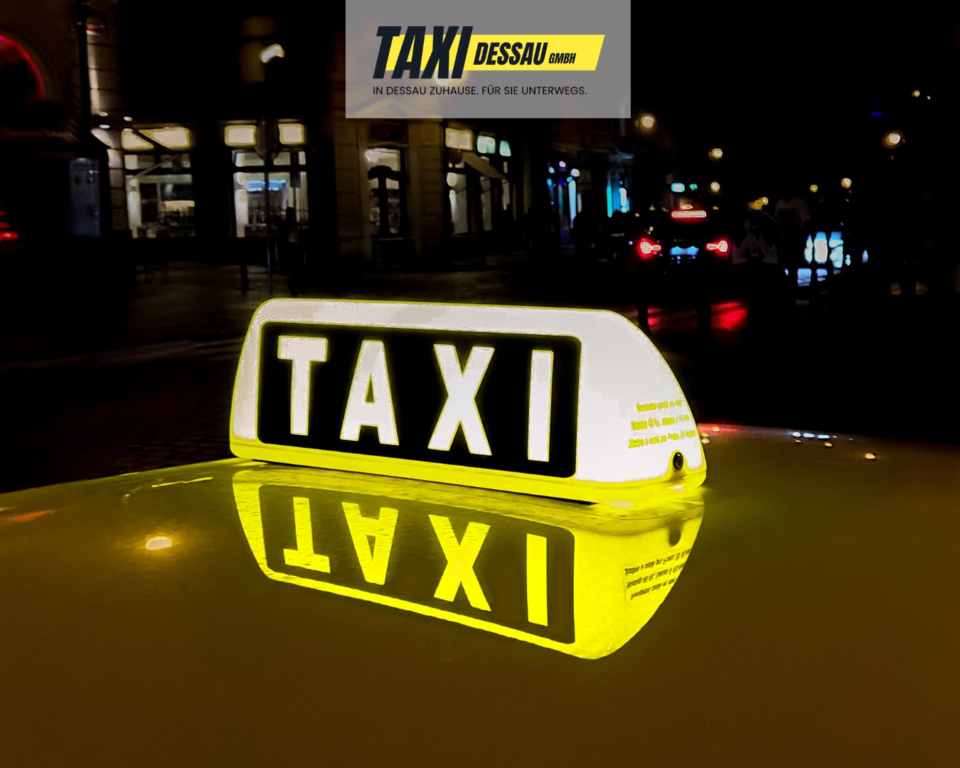 Beleuchtetes Taxi-Dessau-Schild auf einem Taxidach bei Nacht in der Dessauer Innenstadt